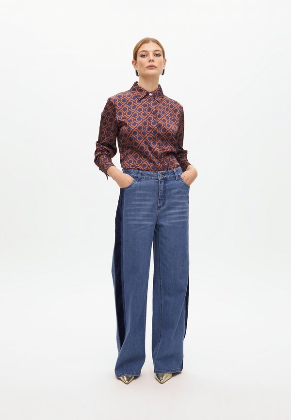 Camisa de botones marrón con estampado y cuello, combinada con unos vaqueros de pierna ancha en azul claro y zapatos metálicos de punta.