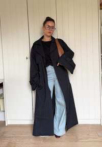 Dlhý námornícky modrý kabát s tenkými pruhmi, veľkými klopami, gombíkmi a širokými rukávmi, nosený cez čierne tričko a svetlomodré džíny. Hnedá kabelka cez rameno.