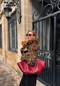 Manteau en fausse fourrure à imprimé léopard, accents noirs, sac en cuir rouge surdimensionné, tenant un croissant, cadre urbain en plein air avec pavé en pierre.