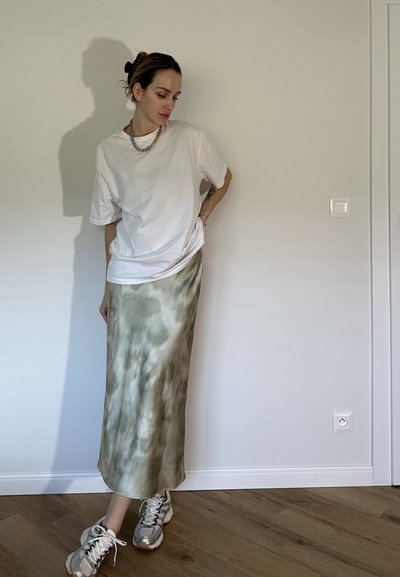 Camiseta blanca de gran tamaño, falda maxi de tie-dye color verde oliva y zapatillas gris. Diseño simple. Textura suave. Accesorios minimalistas.