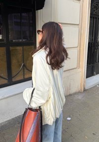 Világossárga, redőzött dzseki kék farmerrel; nagy, többszínű szegecses táskával, kontrasztos pántokkal.