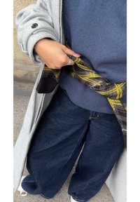 Szary płaszcz, niebieski sweter o fakturze, szerokie ciemne spodnie dżinsowe oraz czarny szalik w kratę z żółtymi akcentami, warstwowo nałożone dla ciepła.