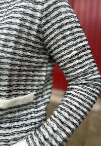 Strikket genser med et horisontalt stripemønster i svart og hvitt. Har rund hals og kontrasterende hvit kant nederst.