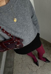 Pull en tricot gris, jupe noire, collants bordeaux, chaussures à talons noires. Sac à main marron et bordeaux avec détails de fermeture éclair et de bandoulière.