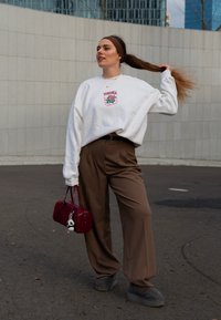 Λευκή φόρμα με μπροστινή γραφική εκτύπωση, καφέ φαρδιές παντελόνες, γκρι σουέτ μπότες μέχρι τον αστράγαλο και μπορντό τσάντα χειρός με μπρελόκ. Άνετο αστικό ντύσιμο.