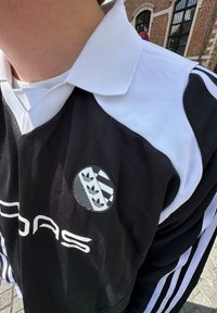 Fekete-fehér sportmez, galléros kialakítással, függőleges csíkokkal, és egy Adidas logóval a bal mellkason, három leveles ikon mellett.