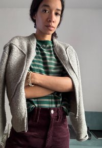 Grå zip-up jakke over en grøn stribet skjorte, parret med burgunder kordfløjlsshorts med en frontknap. Subtil tekstur og farvekontrast.