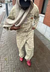 Τζάκετ και παντελόνι από τζιν με καμουφλάζ σε μπεζ χρώμα, συνδυασμένα με ένα ανοιχτό γκρίζο κασκόλ και κόκκινες αθλητικές μπότες. Μαύρο καπέλο με διακοσμητικά στοιχεία.