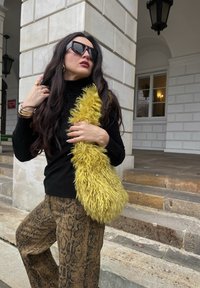 Čierny sveter s rebrovanou štruktúrou, žltá chlpatá kabelka a nohavice s hadím vzorom. Prostredie zahŕňa kamenné schody a stenu s piliermi.