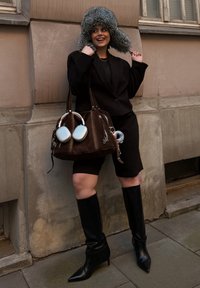 Svart oversized blazer, svarte shorts, knelange svarte skinnstøvler, brun håndveske med sølvdetaljer og en grå pelslue.