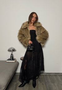 Veste en fausse fourrure beige, robe bustier noire avec accents de dentelle, et bottines noires pointues. Petit sac noir matelassé à la main.