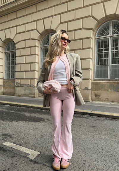 Blazer gris claro sobre una blusa blanca, combinado con pantalones de campana rosas y zapatillas rosas. Los accesorios incluyen gafas de sol y un bolso de peluche rosa.
