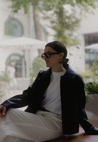 Sort faux læderjakke over en hvid t-shirt, parret med løse cremede bukser. Sorte solbriller og kort hår fuldender looket.