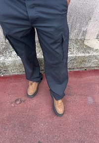 Μαύρες cargo παντελόνες με πλευρικές τσέπες και άνετη γραμμή, σε συν�δυασμό με καφέ σουέτ παπούτσια με καουτσούκ σόλες και ραμμένα διακοσμητικά στοιχεία.