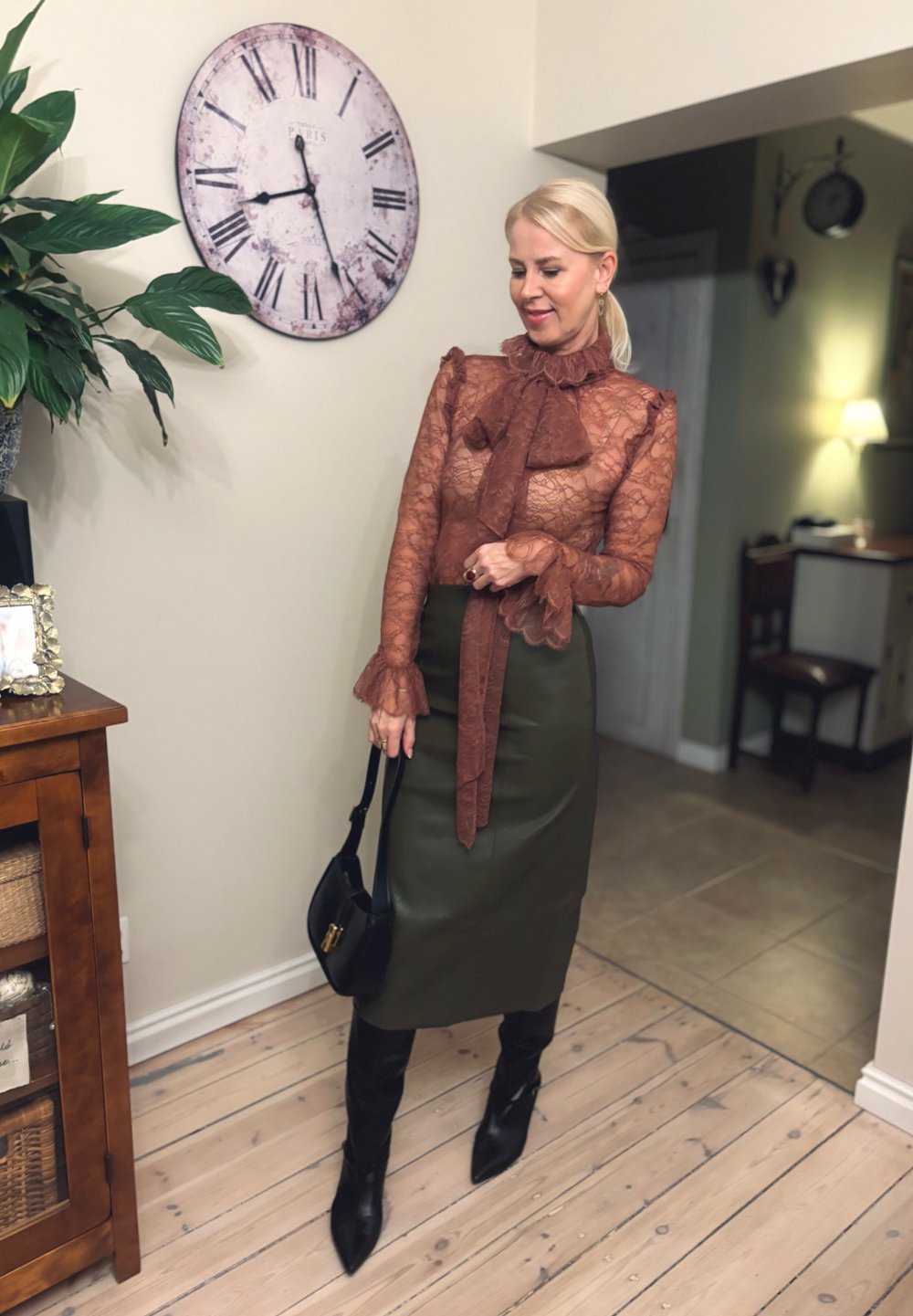 Transparante kanten top in roestkleur, met een strik en gerimpelde mouwen, gecombineerd met een nauwsluitende olijfgroene rok en zwarte laarzen tot boven de knie.