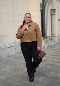 Bruine suède cropped jas met rits aan de voorkant, twee borstzakken; donkere denim hoge taille broek; kleine bruine handtas met een gouden accent.