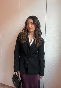 Černé sako na jedno zapínání, doplněné bílou košilí a fialskou sukní. Drž�í černou kabelku. Hladká textura a přizpůsobený střih.