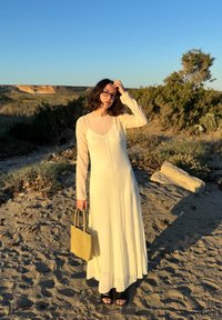 Rochie lungă, din material ivoire, cu mâneci lungi și decolteu rotund; asortată cu o geantă de umăr mică, de culoare verde măslin, și sandale negre.