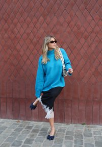 Za duży turkusowy wełniany sweter, czarna spódnica z koronkową lamówką oraz granatowe baleriny z kokardką, na tle teksturowanej, rdzawej ściany.