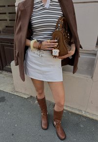 Stripet polo skjorte, hvit skjørt, brun blazer, brune knelengde støvler med metallbeslag, brun håndveske med utskjæringer, nøkkelring formet som toast.