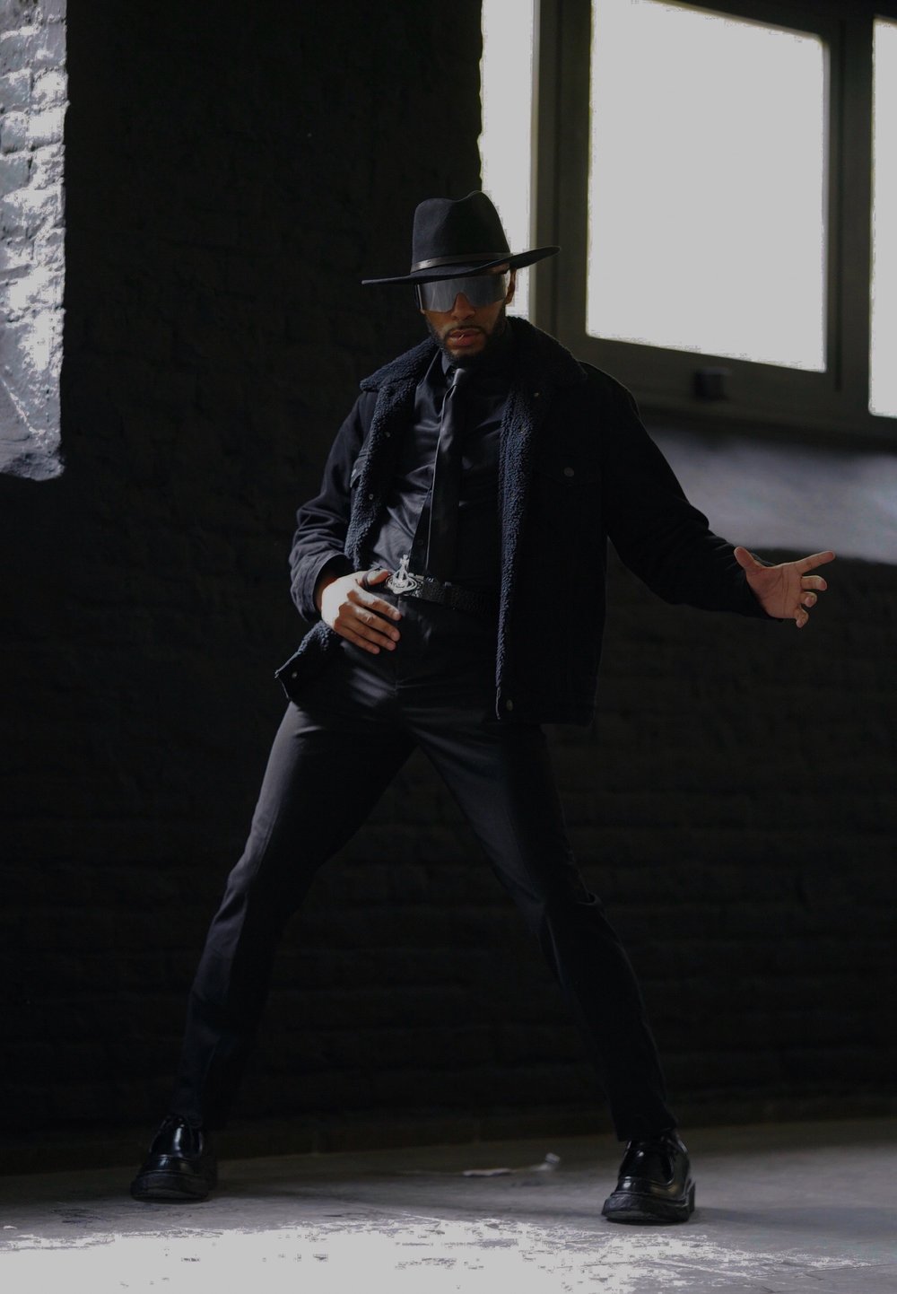 Μαύρο σακάκι από μείγματα μαλλιού με λεπτομέρειες από γούνα, στενή μαύρη μπλούζα, παντελόνια και γυαλιστερά παπούτσια. Καπέλο με φαρδύ γείσο και σκούρα γυαλιά ηλίου.