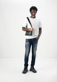 White t-shirt, dark blue jeans, and black sneakers. Black crossbody bag with embossed "DIESEL" logo, smooth fabric, set against a white background.