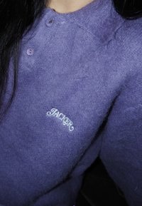 Violets adīts džemperis ar teksturētu audumu, divām pogām pie apkakles un baltu izšuvumu ar tekstu "JACKER."