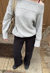 Pull gris à col bateau avec poignets côtelés, associé à un pantalon noir à jambes larges. Un sac à main à motif pend de l'épaule.