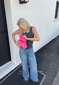Fuchsia quiltet håndveske med kjede-stropper, brukt åpen, holdt av en person i en grå tanktop med sølvnagler og vide blå jeans.