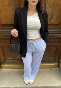 Μαύρο σακάκι πάνω από λευκό ψηλόμεσο τοπάκι, μπλε και άσπρο ριγέ φαρδύ παντελόνι, γκρίζες παπούτσια με άσπρες λεπτομέρειες, κρατώντας μια μικρή μαύρη τσάντα.