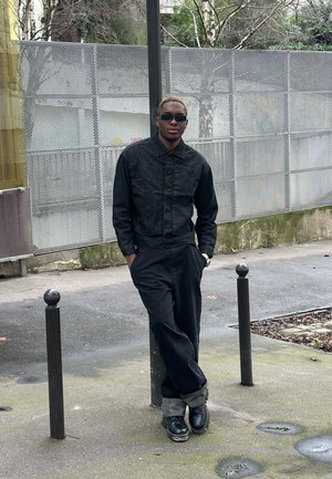 Chaqueta de mezclilla negra, pantalones negros y botas de cuero negras. Los detalles notables incluyen un cuello con solapa y puños enrollados con un patrón gris.