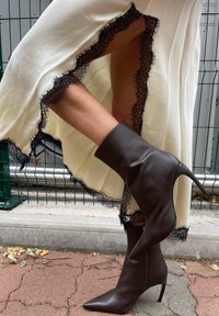 Bruine leren enkellaarsjes met een spitse neus en een stilettohak, gecombineerd met een witte jurk met een zwarte kantafwerking.