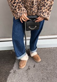 Καφέ σουέτ παντόφλες με αφράτη λευκή επένδυση, υπερμεγέθη μπλε τζιν παντελόνια και μαύρη τσάντα χιαστί με ασημί αλυσίδα.