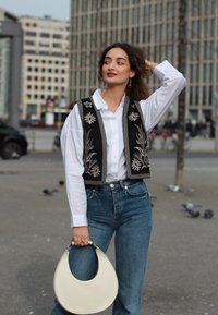 Črno vezeno telovnik nad belo srajco, v kombinaciji z visokimi modrimi kavbojkami. Nosila je belo krožno torbico.