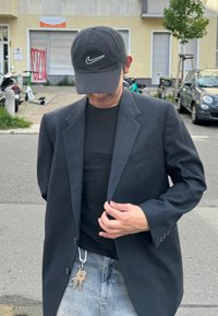 Črn blejeni blazer z dvema zaznamkama, nosi se preko oprijetega črnega srajčnega. Vidna sta tudi črna kapa in ključi pritrjeni na zanko pasu.