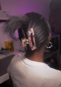 Femme aux cheveux noirs attachés en une queue de cheval lâche maintenue par un grand clip à cheveux multicolore, portant des boucles d'oreilles créoles et une chemise blanche.