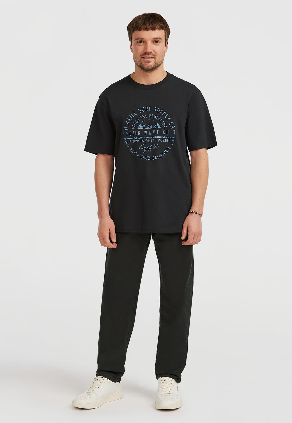 Czarna bawełniana koszulka z krótkim rękawem, z niebieskim tekstem graficznym i wzorami inspirowanymi oceanem. W zestawie z ciemnozielonymi spodniami i białymi sneakersami.