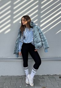 Light blue puffer jacket, patterned blue sweatshirt, black leggings, white socks with black stripes, and reflective trainers.