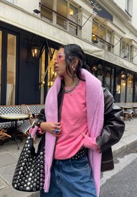 Čierna kožená bunda, ružový fleece šál, ružová mikina, modré džínsy, čierna kabelka s cvočkami, ružové slnečné okuliare, metalické doplnky.