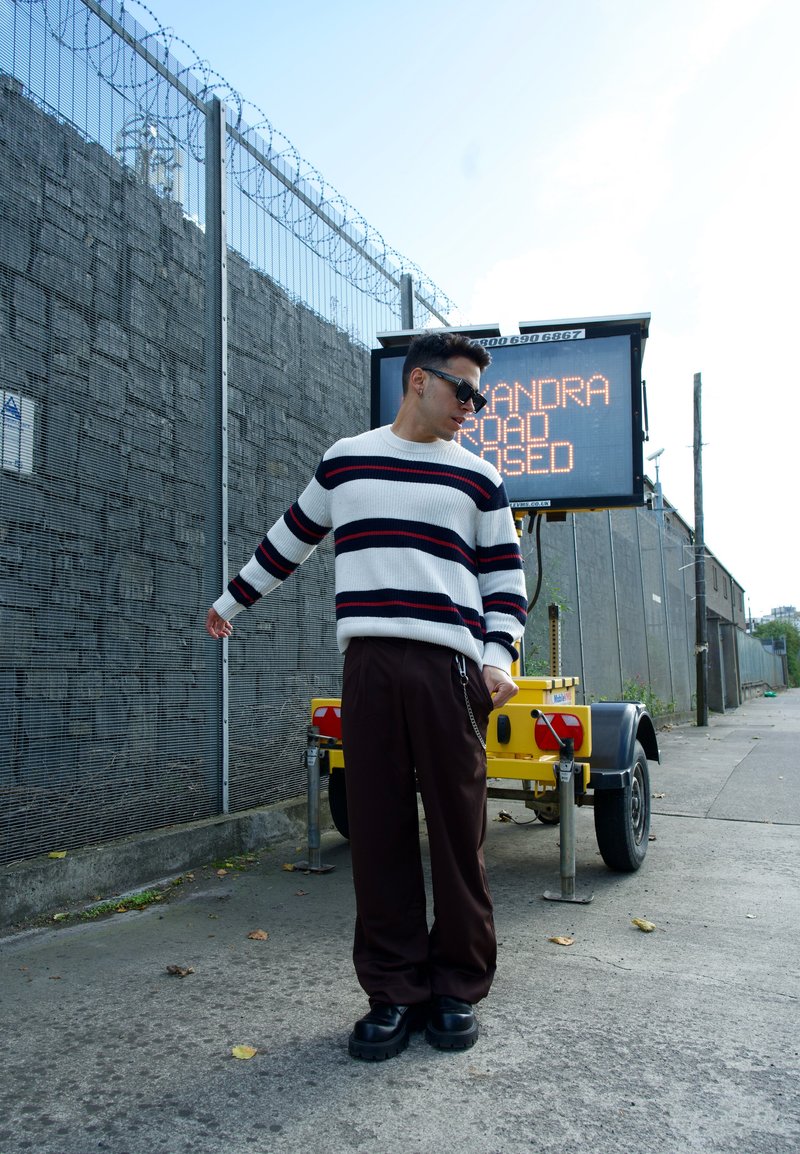 Maglione a maglia con righe orizzontali nere e rosse, abbinato a pantaloni larghi marroni scuri e scarpe platform nere massicce.