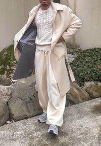 Manteau en laine beige, pull en maille blanche texturée, pantalon crème et baskets grises. Le manteau est doublé de gris et a une coupe décontractée.