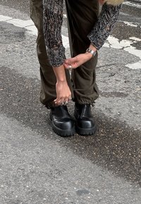 Zwarte plateauboots met dikke rubberen zolen, ronde neuzen en een gladde textuur, gedragen met olijfgroene joggerbroeken en een gemêleerd shirt.