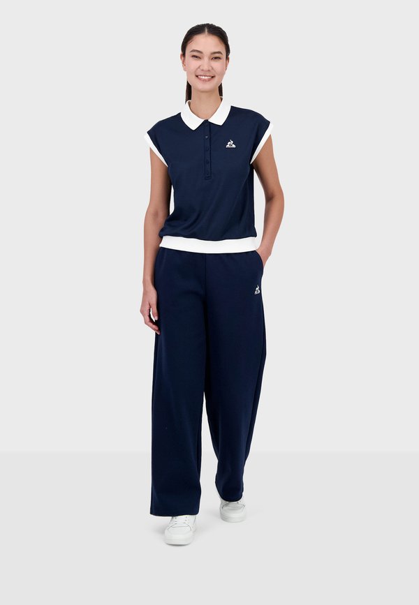 Polo de manga corta azul marino con cuello blanco, tapeta de botones y logo; combinado con pantalones de pierna ancha azul marino; zapatillas blancas. Textura de tela suave.