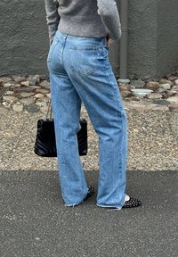 Jeans azzurri chiari a vita alta con design a gamba dritta. Il tessuto ha una texture sbiadita; tasche posteriori con patta molto evidenti. Indossati con ballerine nere a pois.