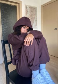 Sudadera de algodón marrón y joggers a juego, con un corte relajado, puños y capucha, combinados con zapatillas blancas y calcetines azul claro.
