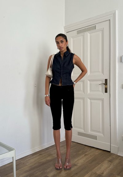 Top sin mangas de denim con un diseño ajustado en azul oscuro, combinado con pantalones cortos negros. Sandalias de tacón transparente completan el look.