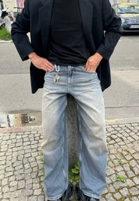 Črni blazer s pinstripes vzorcem nad črnim majico, v kombinaciji z zbledelimi modrimi kavbojskimi hlačami z rahlim prehodom in ključi, pritrjenimi na pasu.