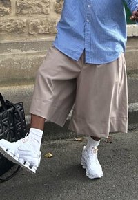 Μπεζ φαρδιά σορτς συνδυασμένα με λευκά αθλητικά παπούτσια και κάλτσες μέχρι τον αστράγαλο. Το τοπ έχει μπλε ριγέ μοτίβο, με άνετη εφαρμογή και σ�τιλ με κουμπιά.