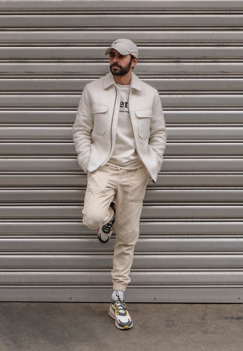 Chaqueta de lana color blanco roto con dos bolsillos frontales, pantalones de pana color beige claro y zapatillas con estampado en rojo, amarillo y negro.