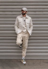 Chaqueta de lana color blanco roto con dos bolsillos frontales, pantalones de pana color beige claro y zapatillas con estampado en rojo, amarillo y negro.